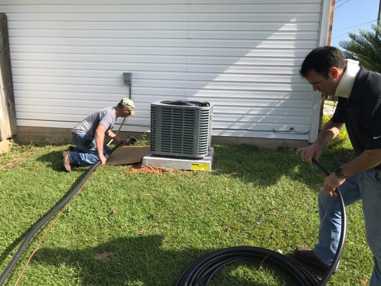 Technicians servicing outdoor HVAC equipment beside a building